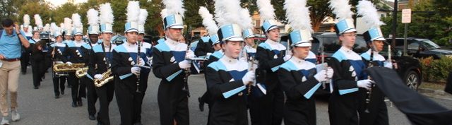 240913 Parade Members of the Yorktown High School Marching Band Woodwind Section parading to the football stadium. Students are wearing their YHS uniforms with black pants, Navy, white, black, and light blue tops and white and black hats with white plumes.