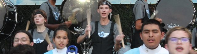 240913 Stand Band Members of the Yorktown High School Marching Band performing in the stands. Two bass drummers and two snare drummers where black overalls with grey YHS band shirts. Other members wear Members of the Yorktown High School Marching Band Brass Section performing the National Anthem. Students are wearing their YHS uniforms with black pants, Navy, white, black, and light blue tops.
